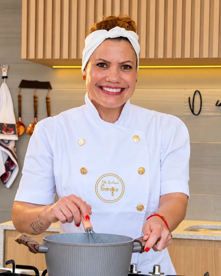 Rita Barhouch sorrindo, de jaleco, mexendo uma panela na cozinha